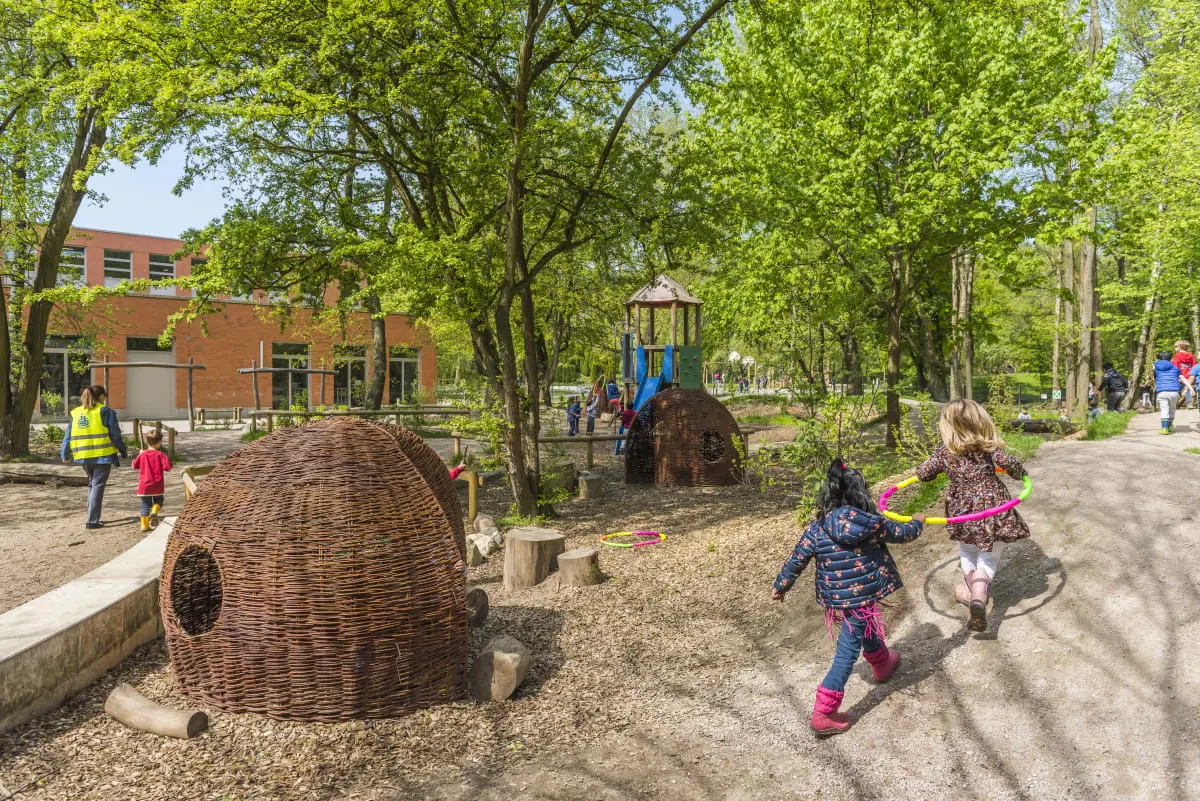 Children playing outdoors near a woven dome structure on the green campus playground