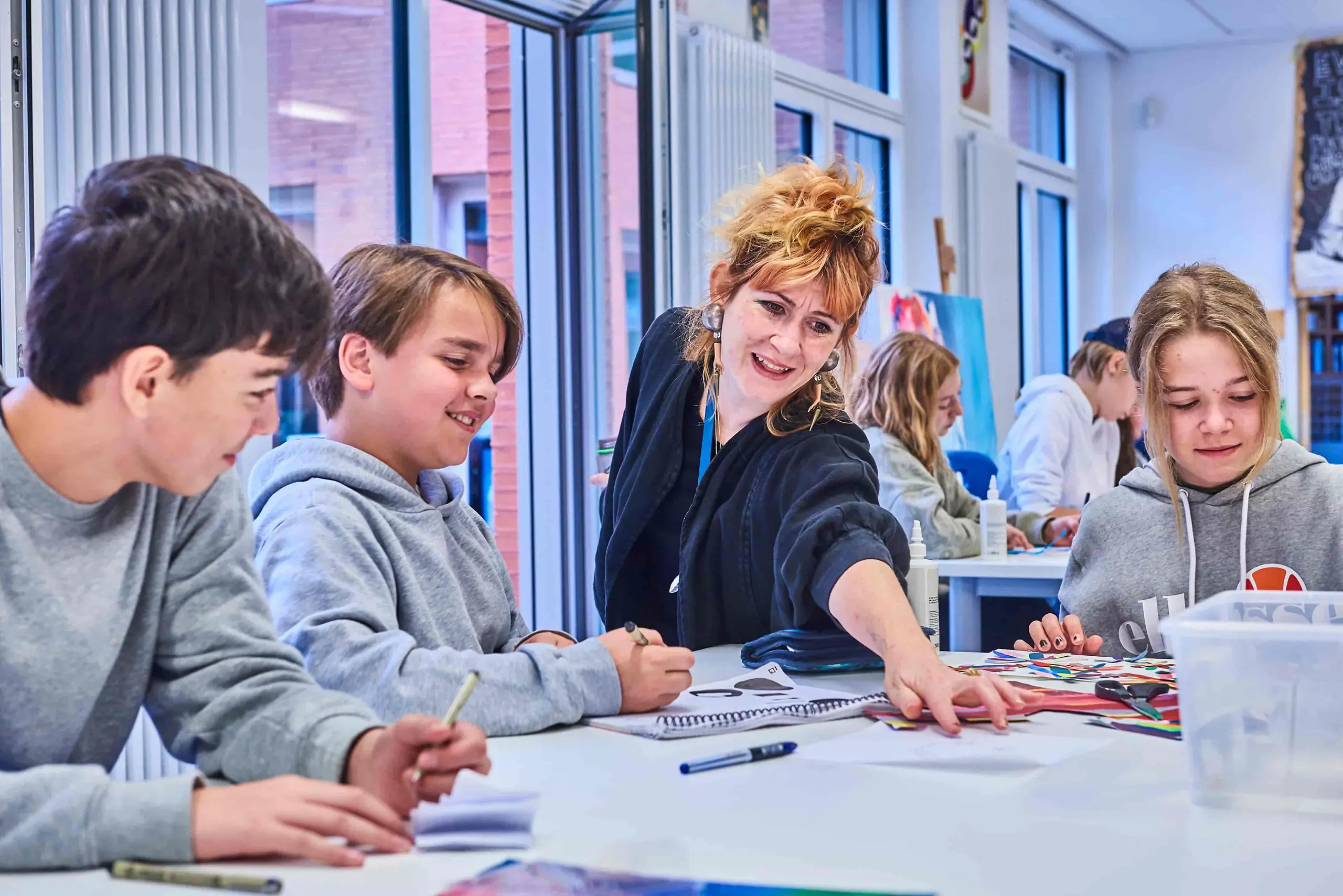 Female teacher smiling while assisting a group of students working together around a classroom table at ISH