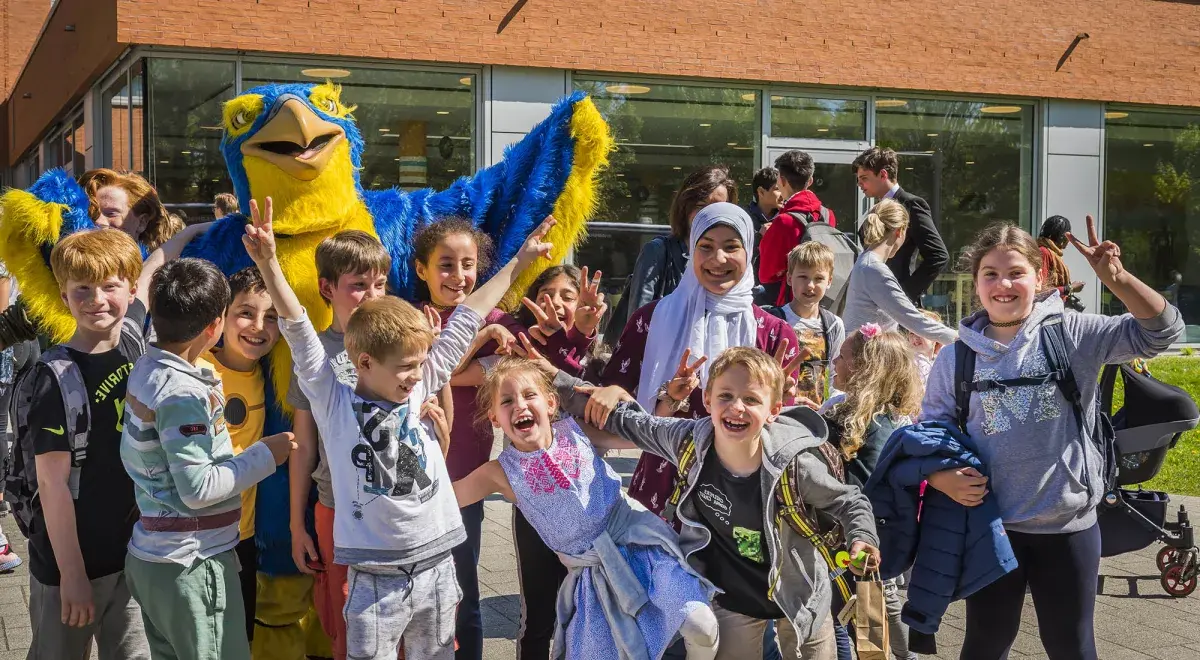 Group of cheering students posing outdoors with the blue and yellow ISH school mascot