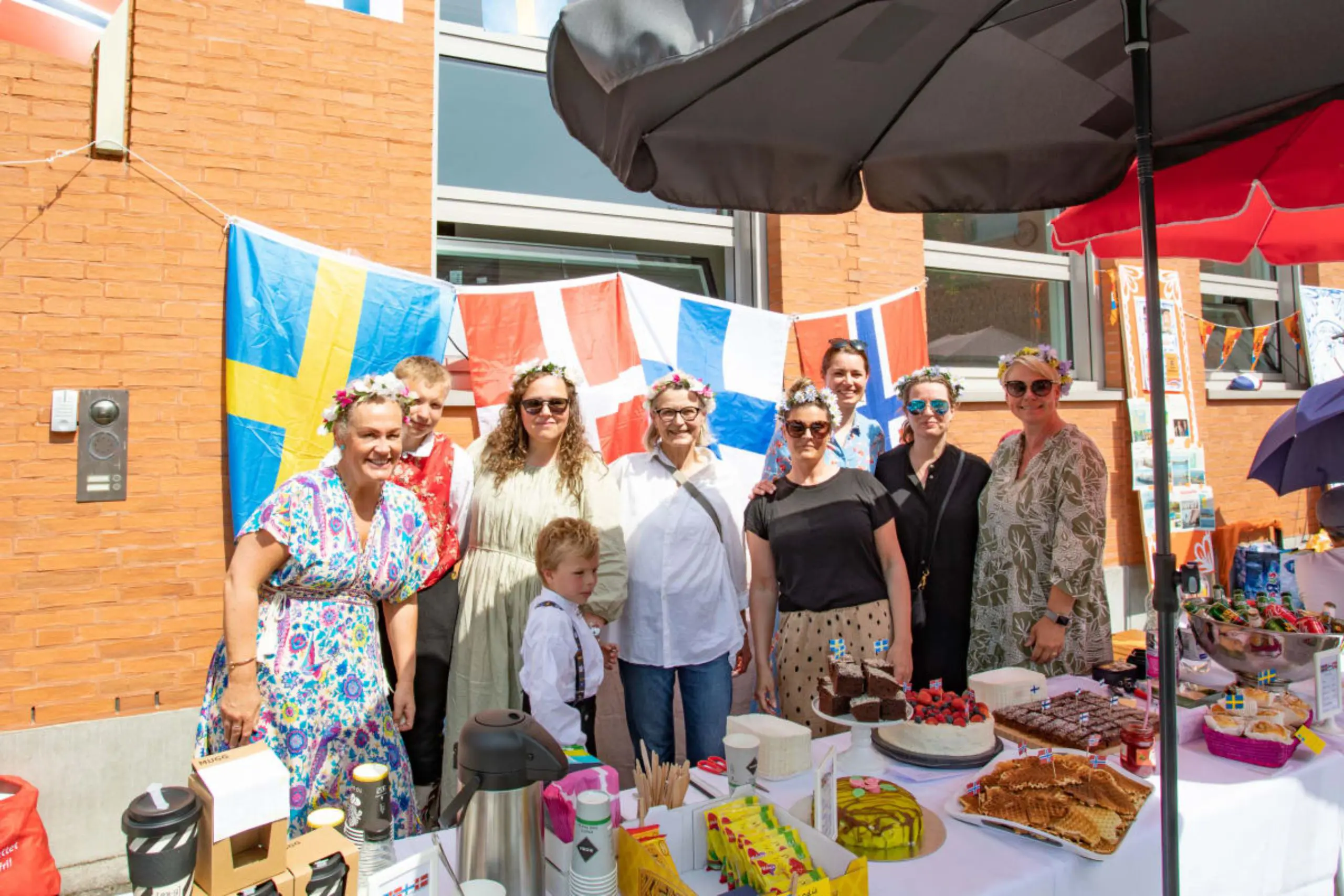 Parents standing together beside a food table decorated with Scandinavian flags during an international community fair