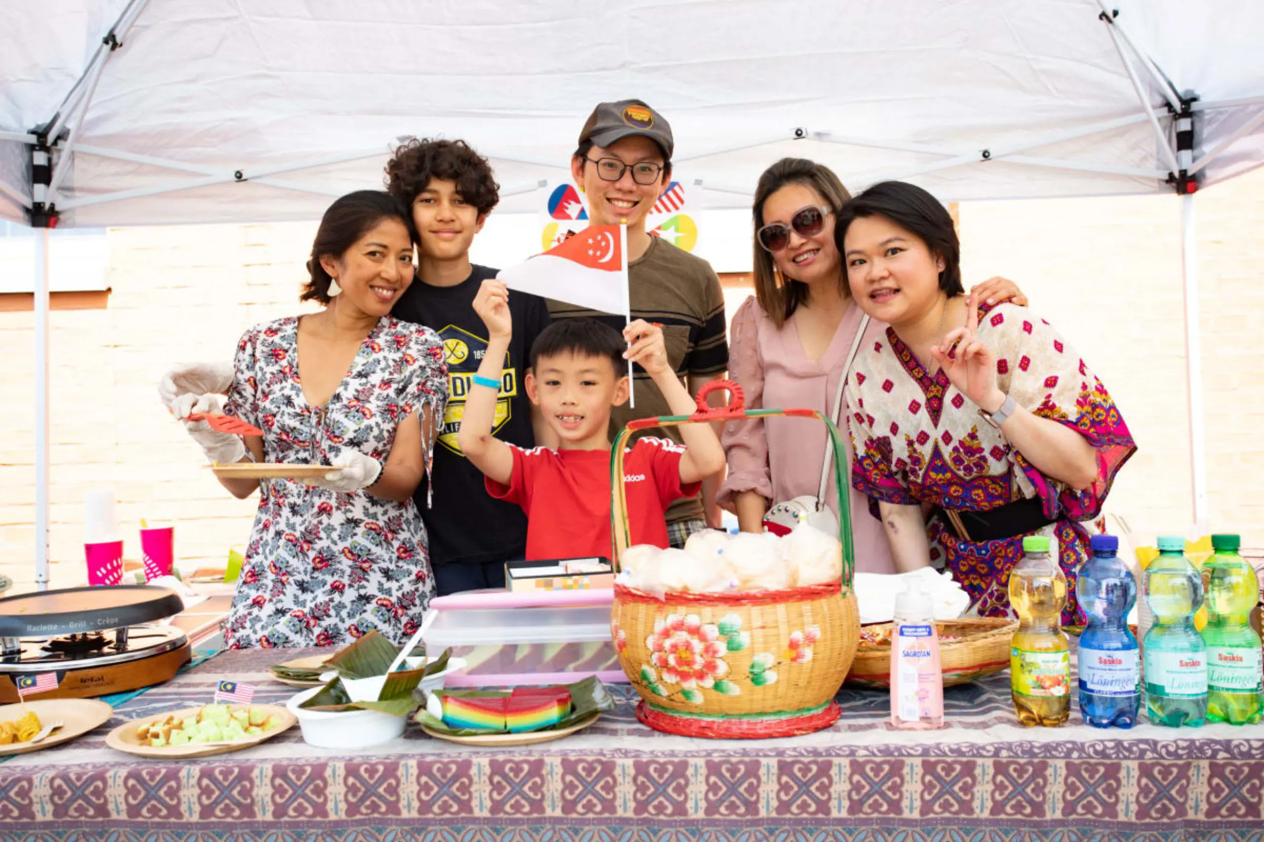 Family standing behind an Asian food stall displaying cultural dishes at a school international festival