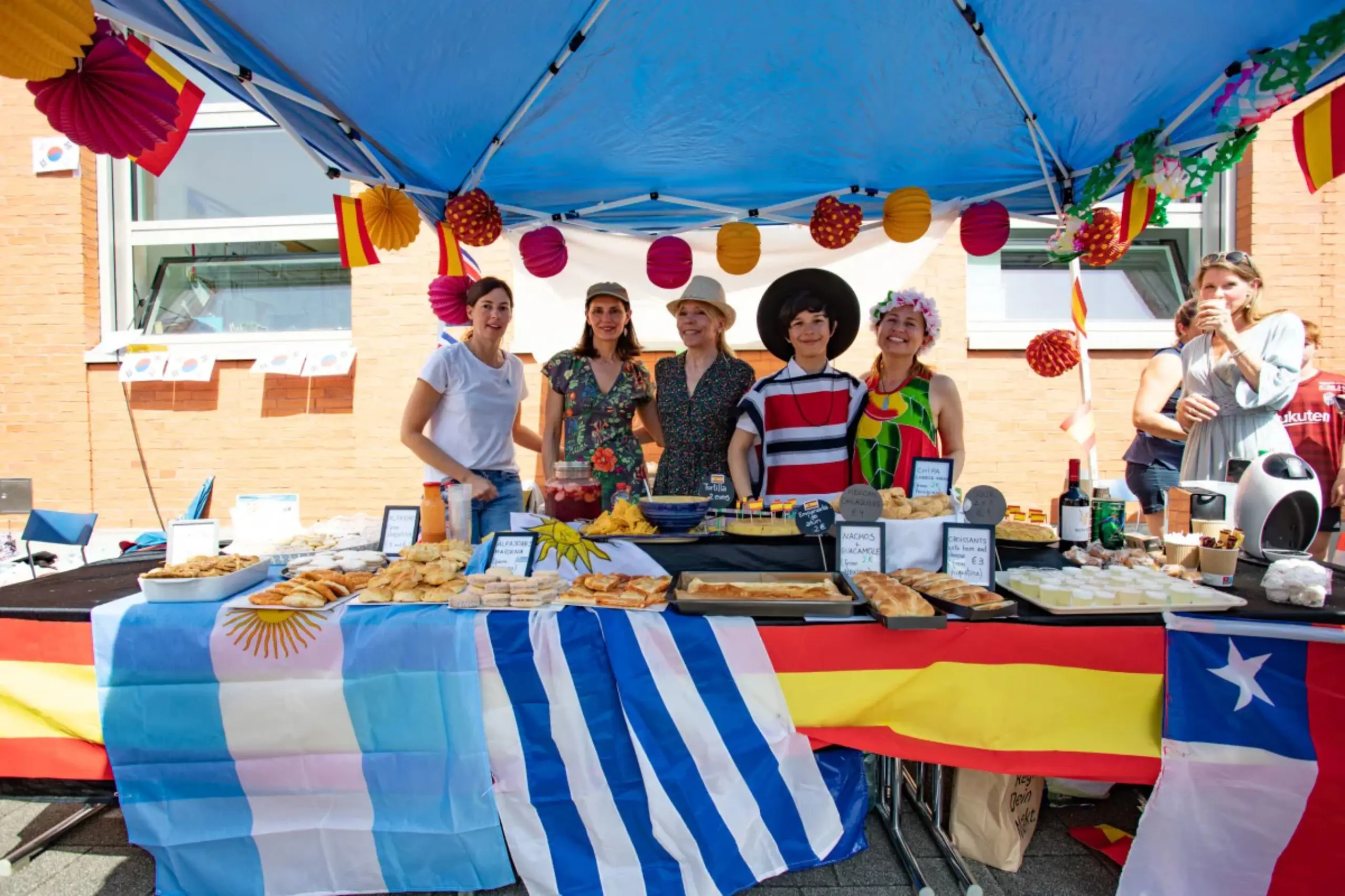 Parents and volunteers gathered behind a South American cultural food booth decorated with national flags