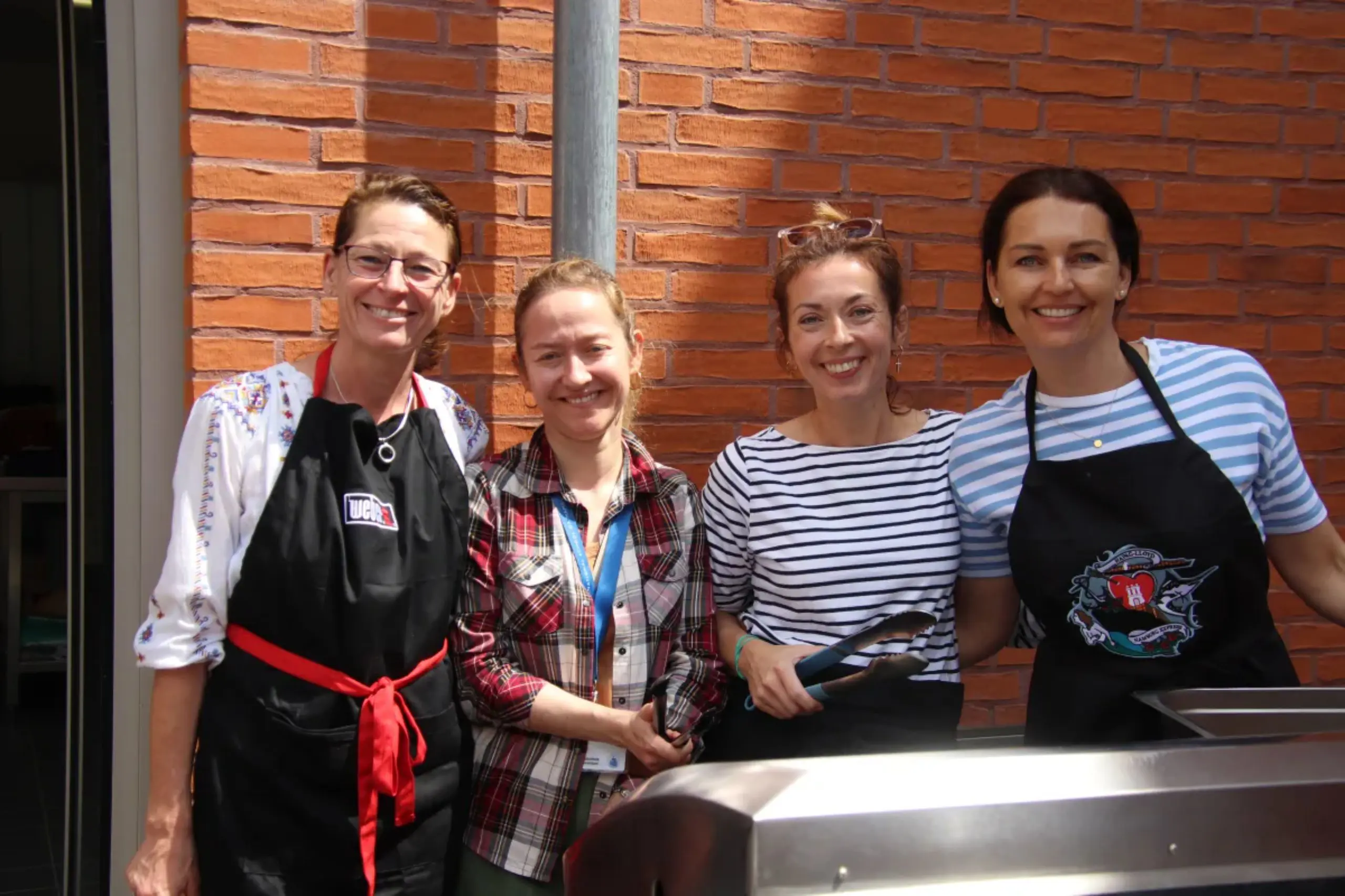 Volunteers wearing aprons smiling at a food station during a school community event