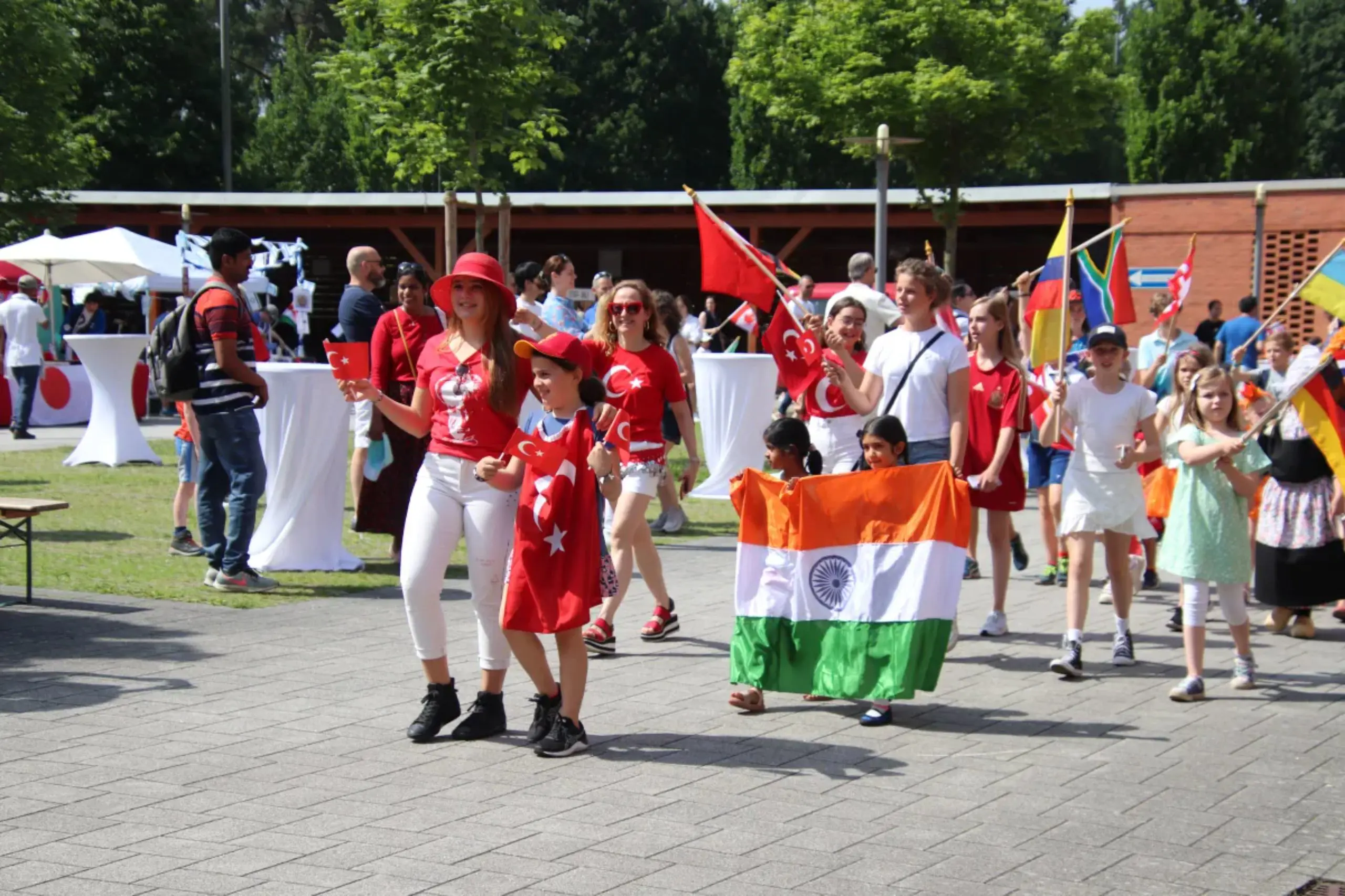 Students and parents wearing traditional attire and carrying national flags during an international cultural parade at ISH