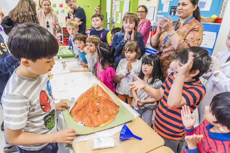 Students gathered around a table clapping during a classroom science experiment