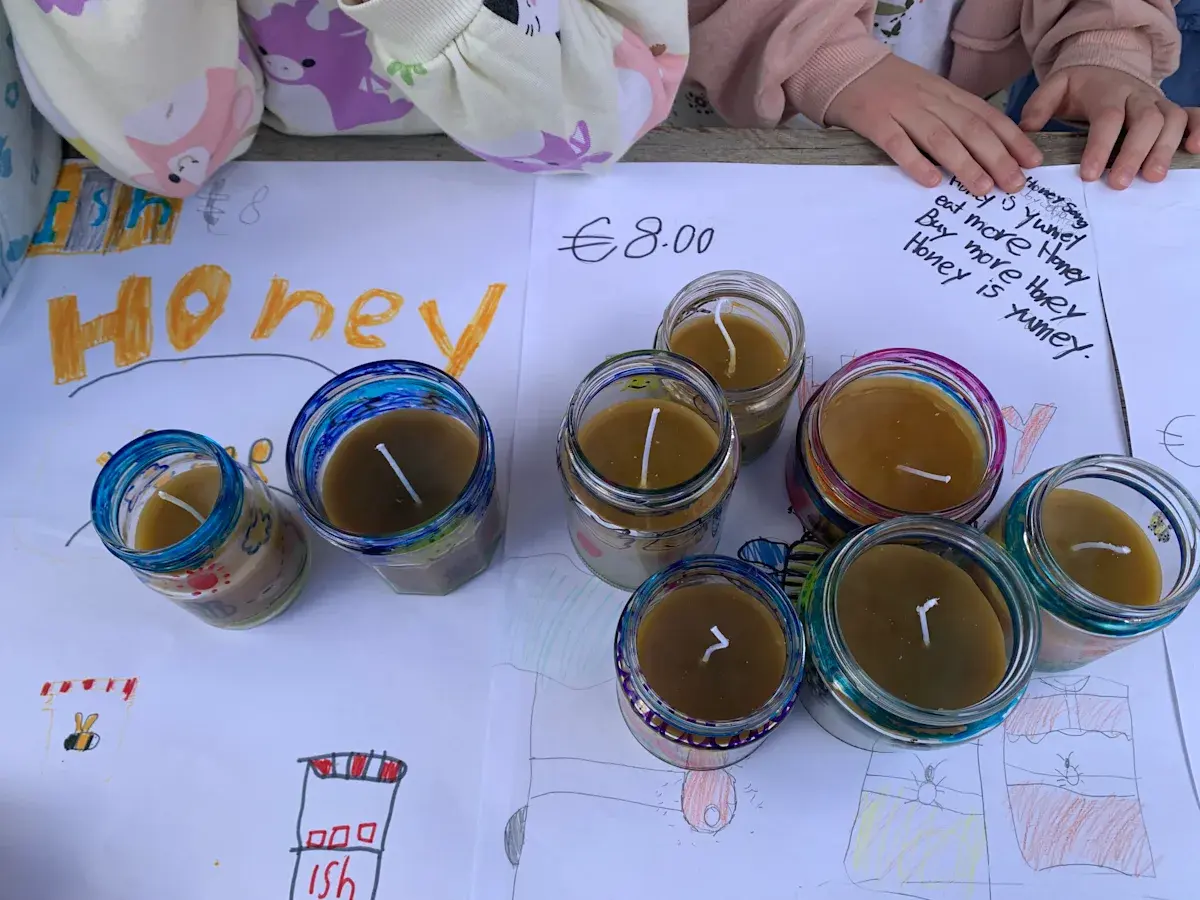 Handmade candles in glass jars labeled Honey sitting on student drawing