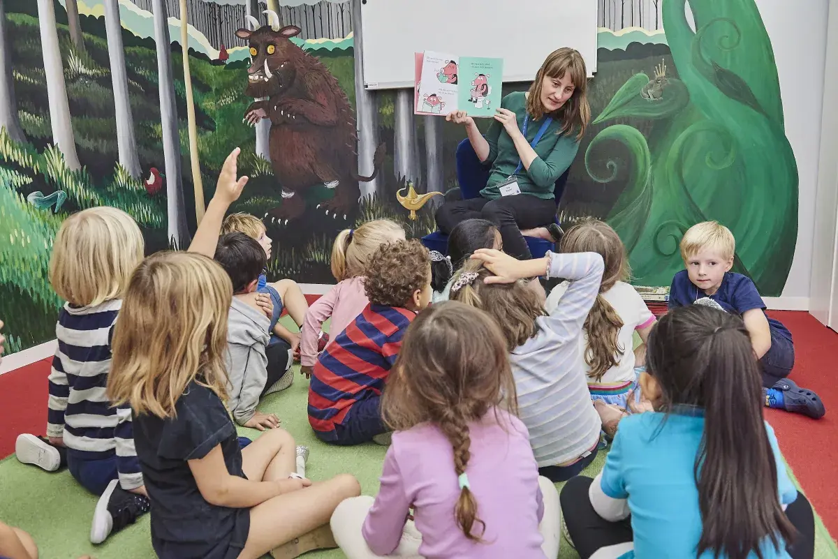 Librarian reading a picture book aloud to a group of seated young students