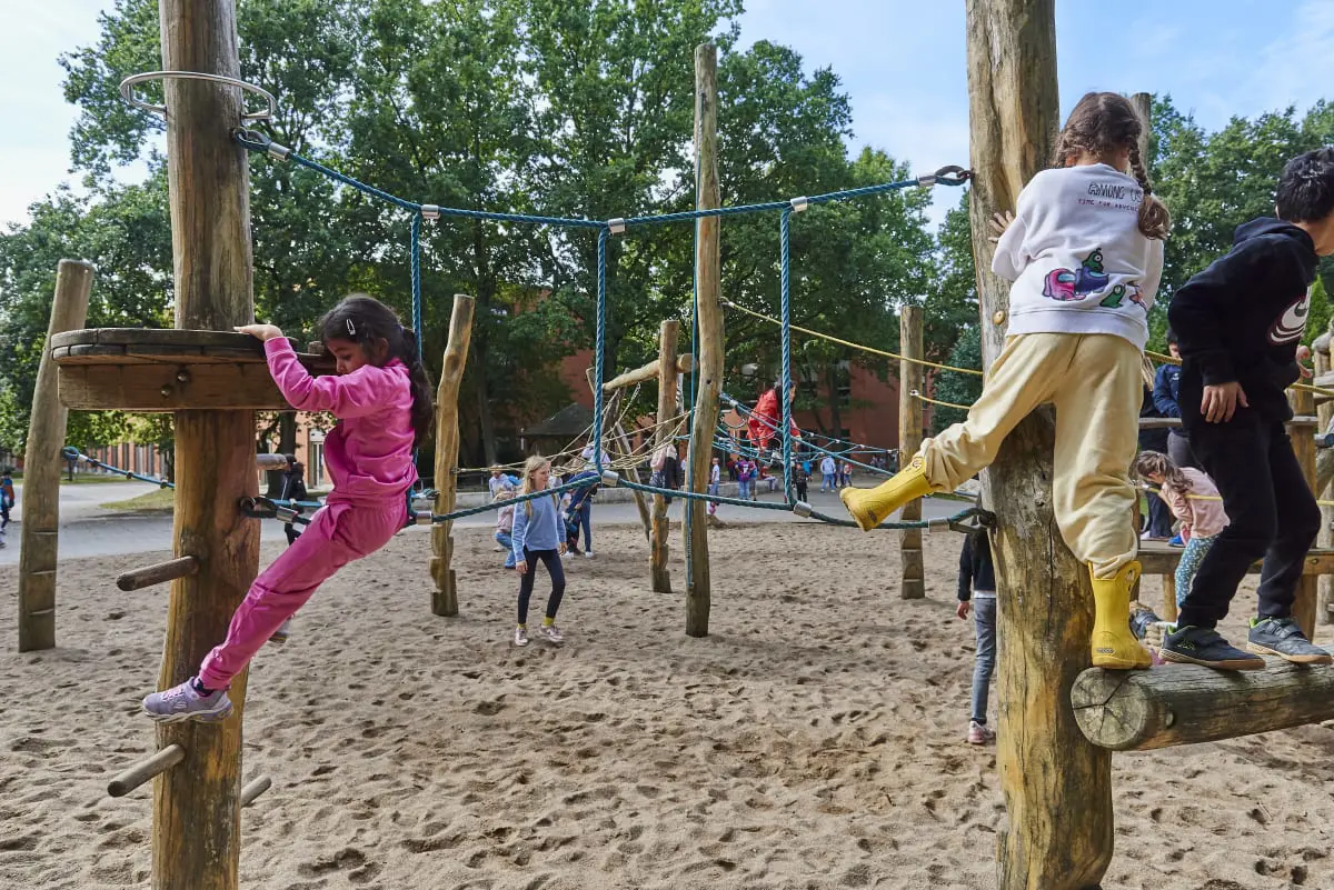 Junior school students playing and climbing on the wooden playground equipment