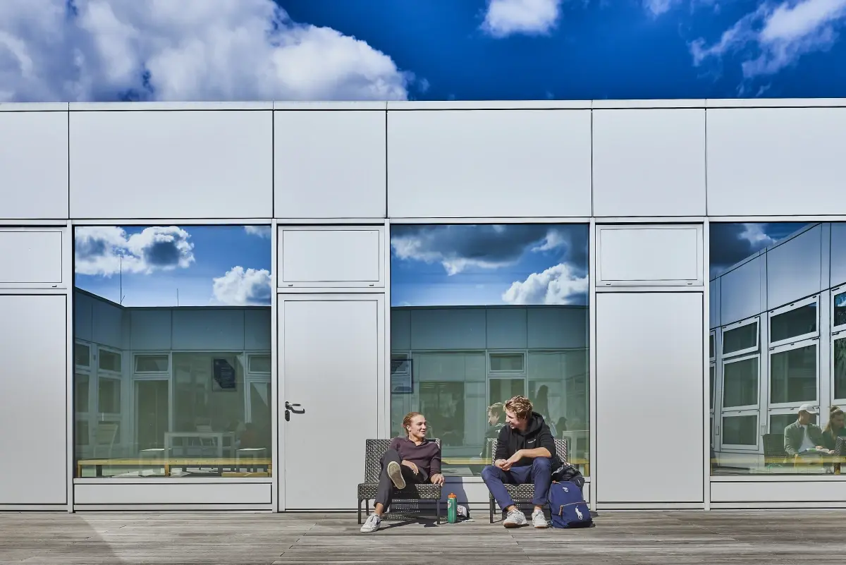 Two students sitting outdoors together in front of the modern International School of Hamburg building exterior