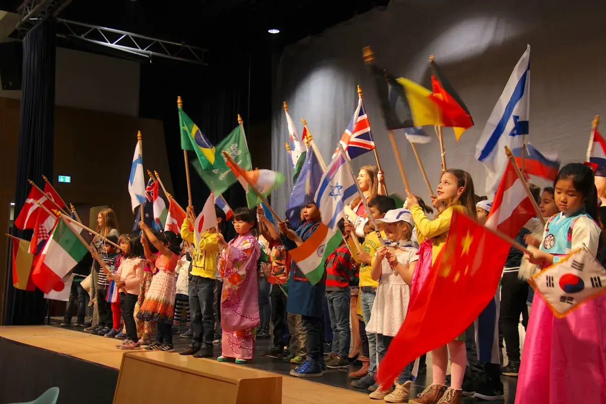 Students waving various national flags on stage during a cultural school event
