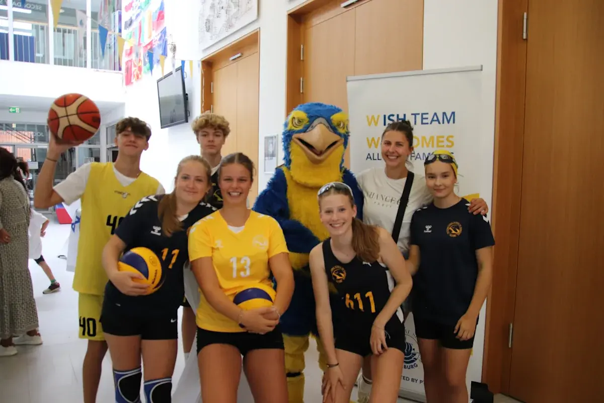 ISH volleyball sports team posing with their mascot in the gymnasium