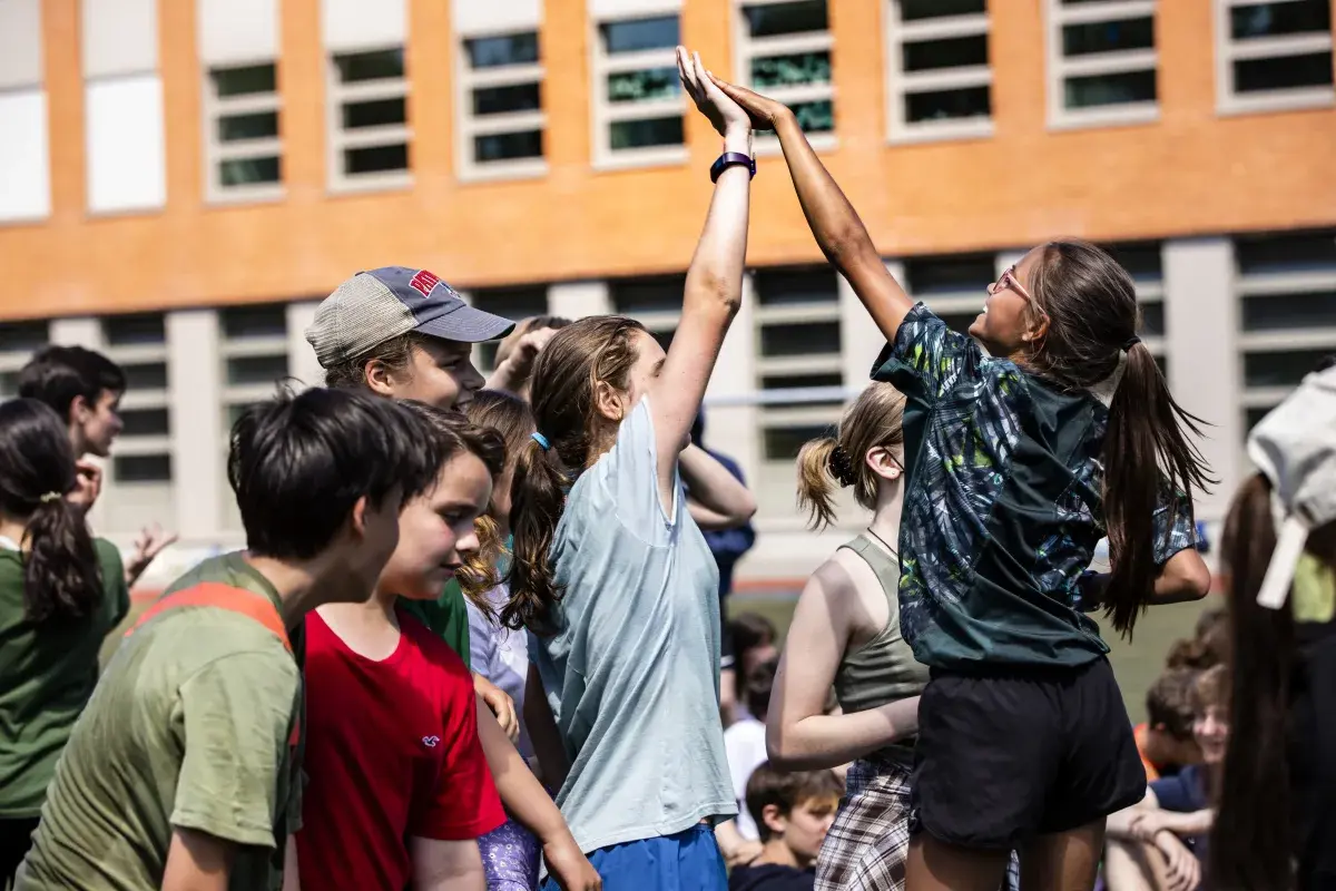 Secondary school students high-fiving outdoors on campus
