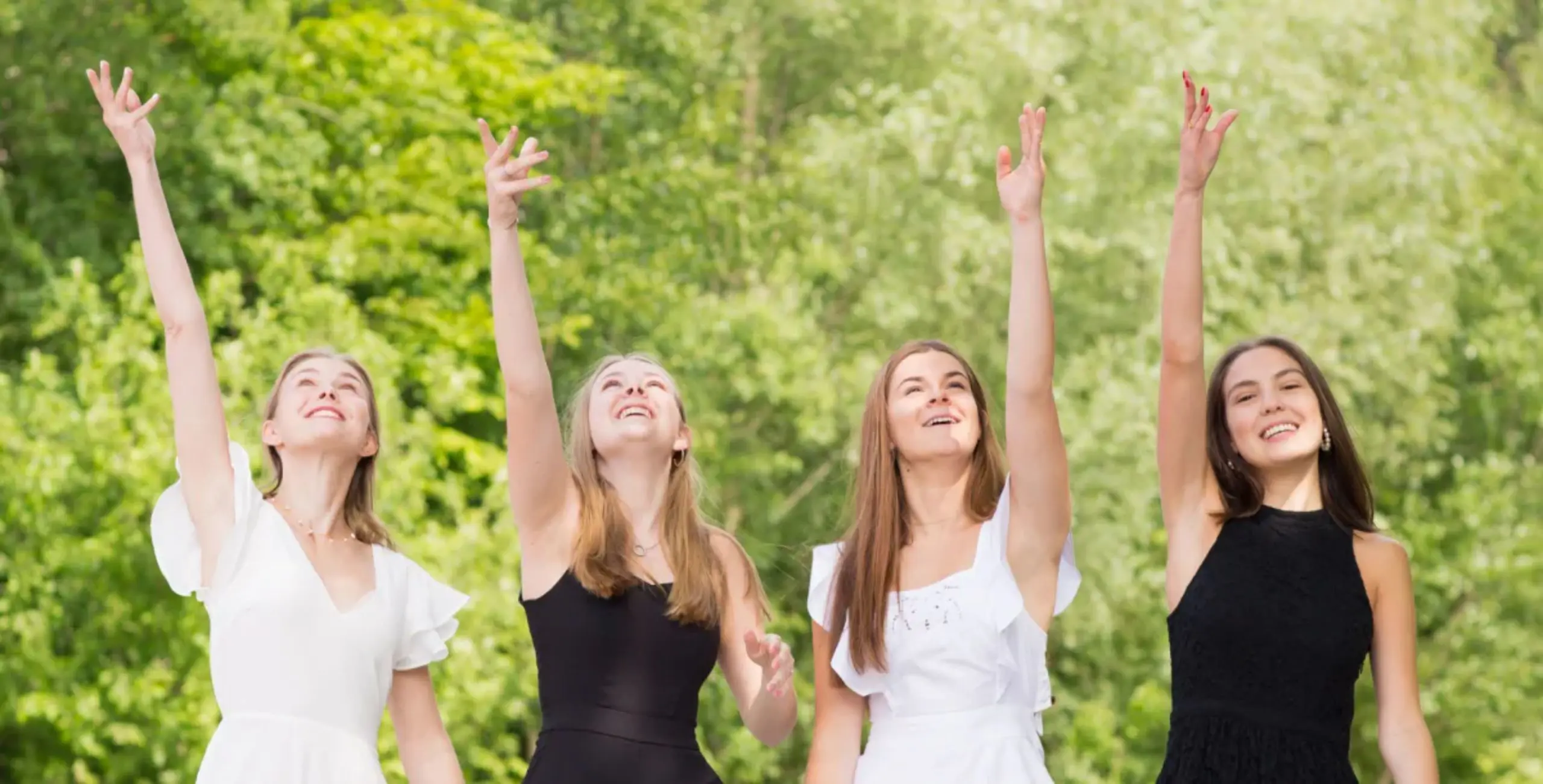 Four graduating students celebrating outdoors with raised hands during a school ceremony