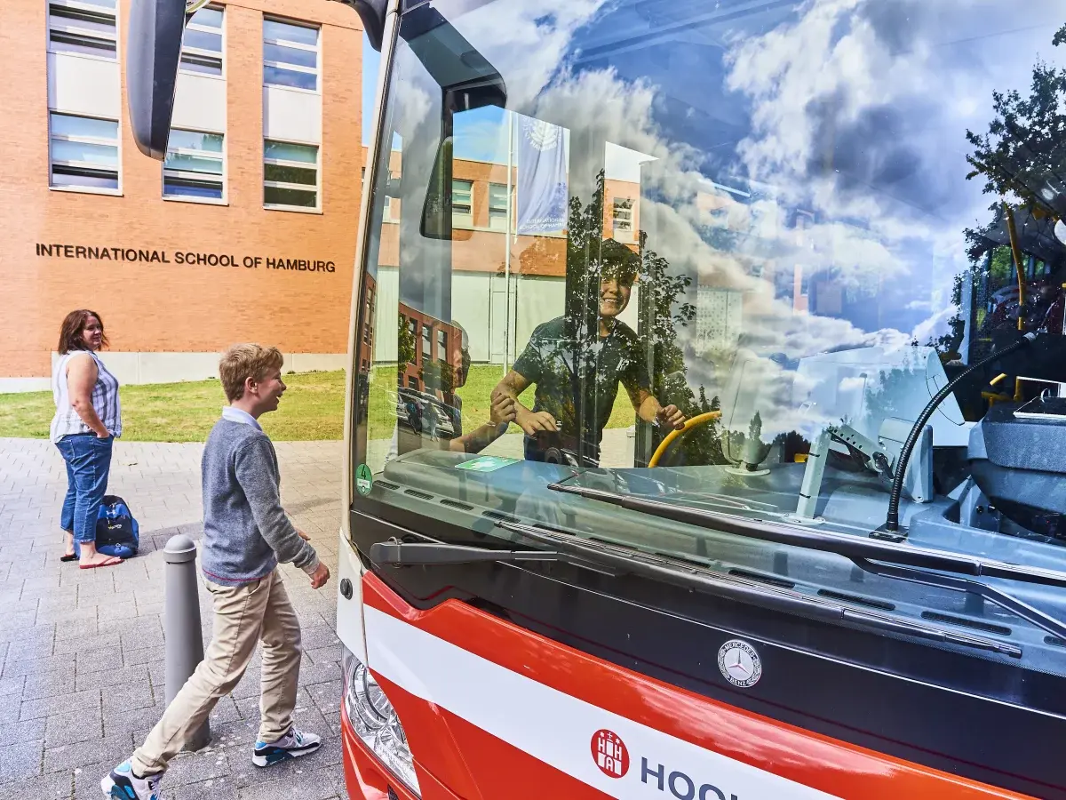 Student boarding the red and white school bus in front of the International School of Hamburg campus
