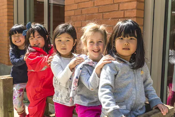 Five young primary school students standing in a line outside the school building